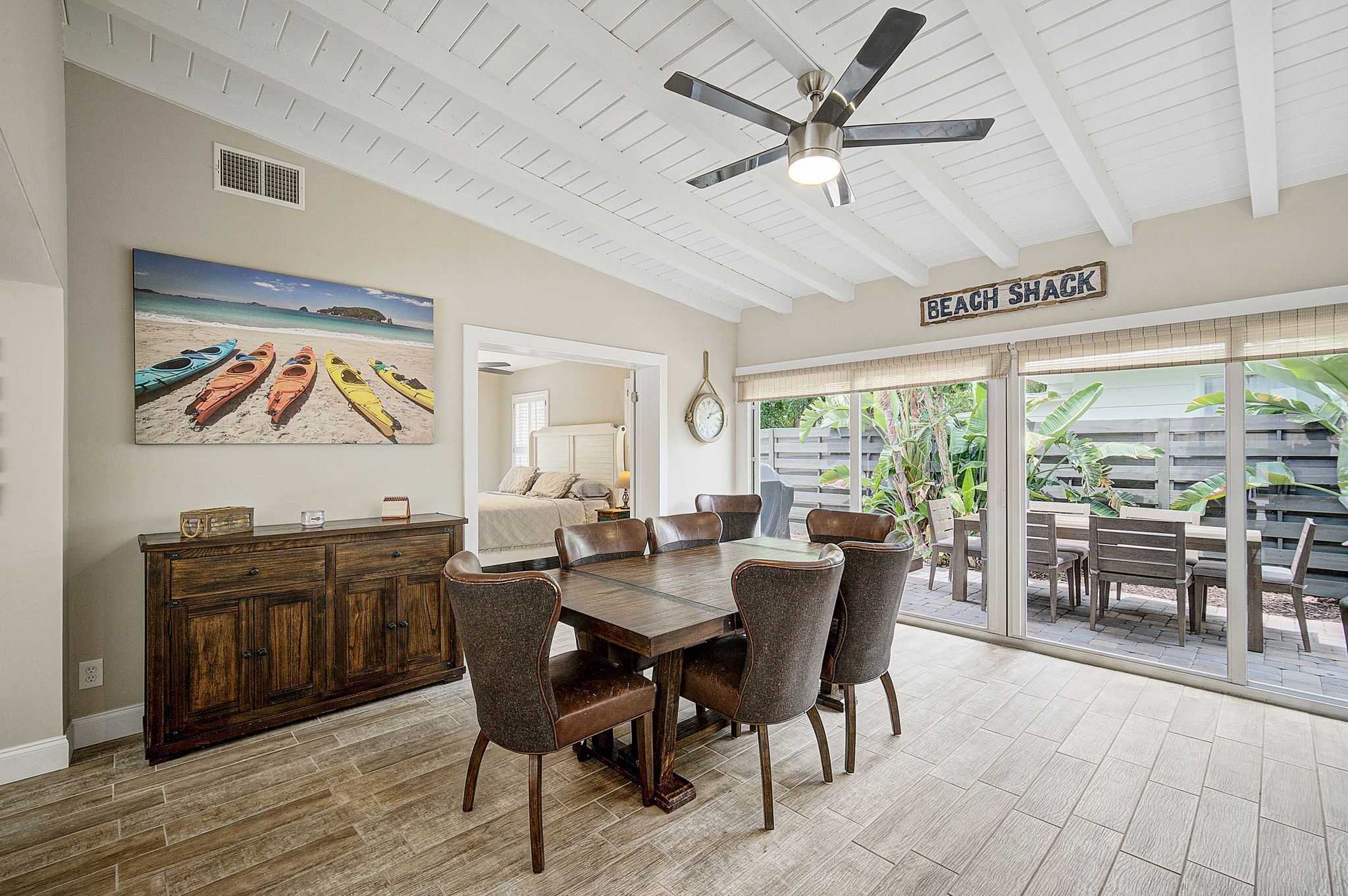 A dining area with a wooden table and chairs, a ceiling fan, and a view of the outdoors.