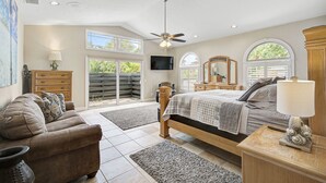 Ein geräumiges Schlafzimmer mit einem großen Bett, einem Deckenventilator, einem Fernseher und Blick ins Freie durch eine Schiebetür.