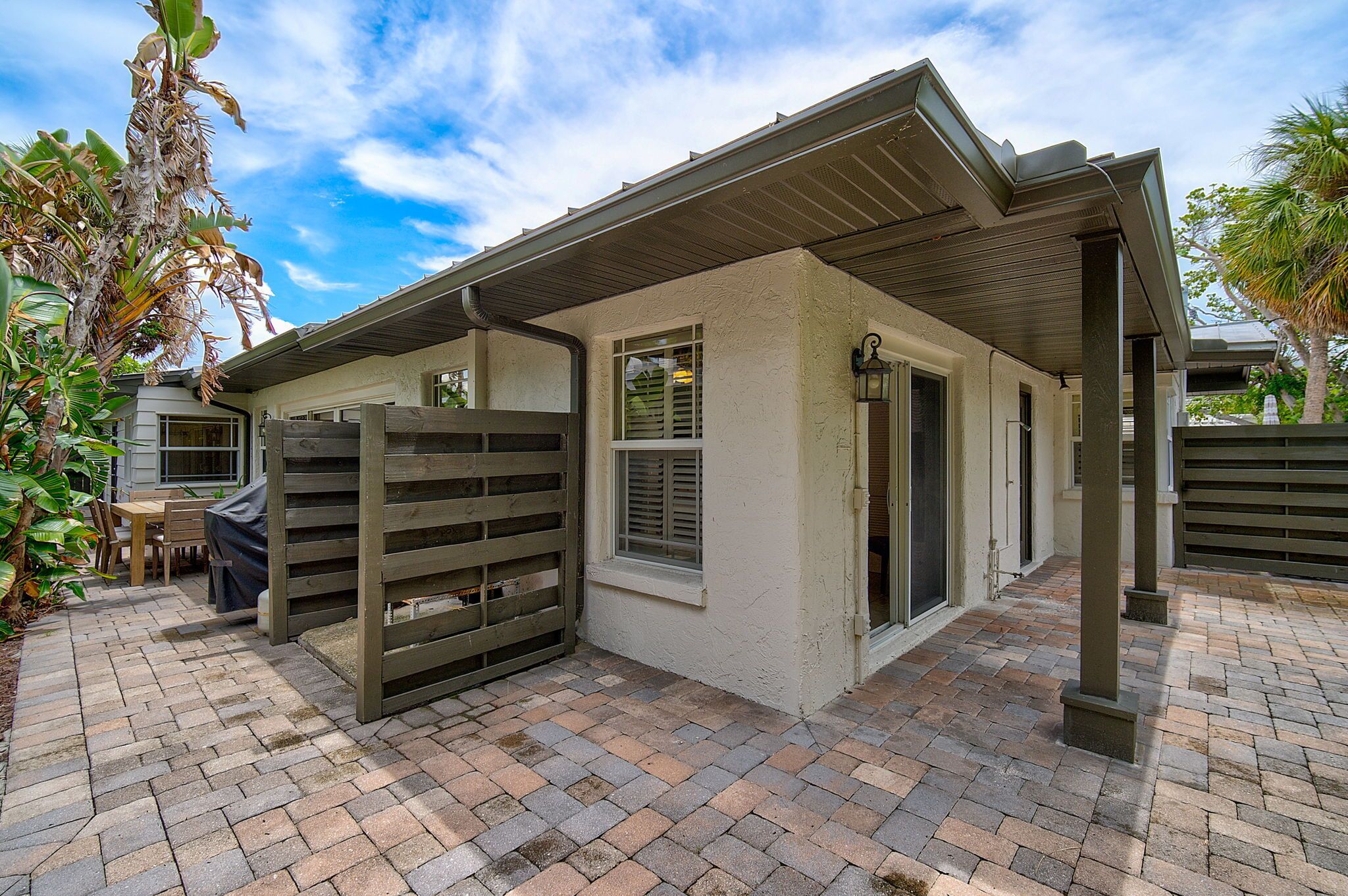 A covered patio area with a brick floor, a wooden fence, and a door leading to an interior space.