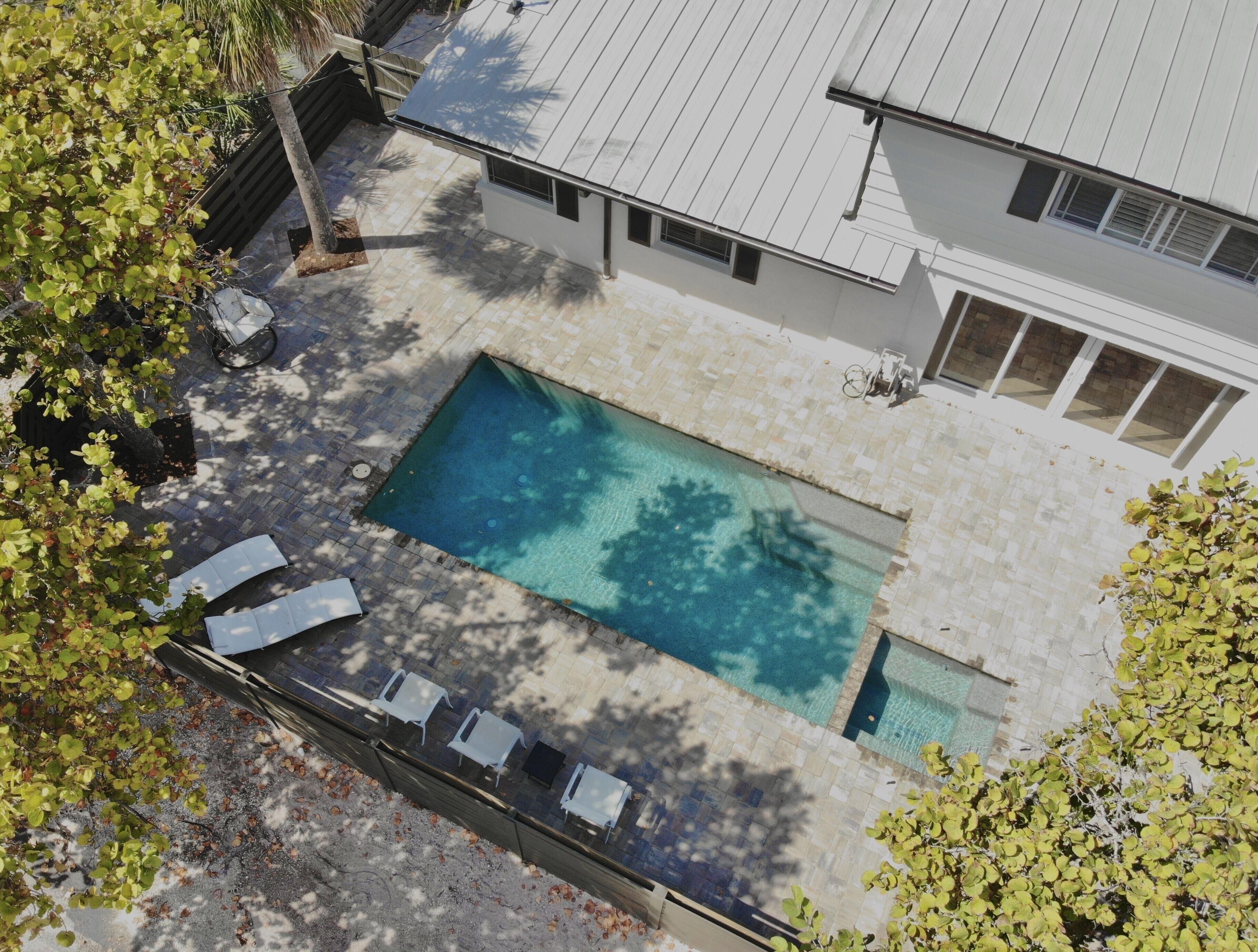 Una piscina rectangular con borde de baldosas, rodeada por un edificio blanco con techo de metal y ventanas.