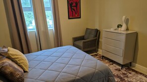 A bedroom with a bed, a chair, a dresser, and a window with curtains.