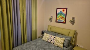 Ein Bett mit gemusterten Betttextilien, einem Kopfteil und dekorativen Kissen. An der Wand hängt ein Kunstwerk, das eine Berglandschaft zeigt.