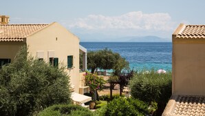 Ein Küstengebäude mit Terrasse, das auf das Meer blickt, umgeben von viel Grün und blauem Himmel.