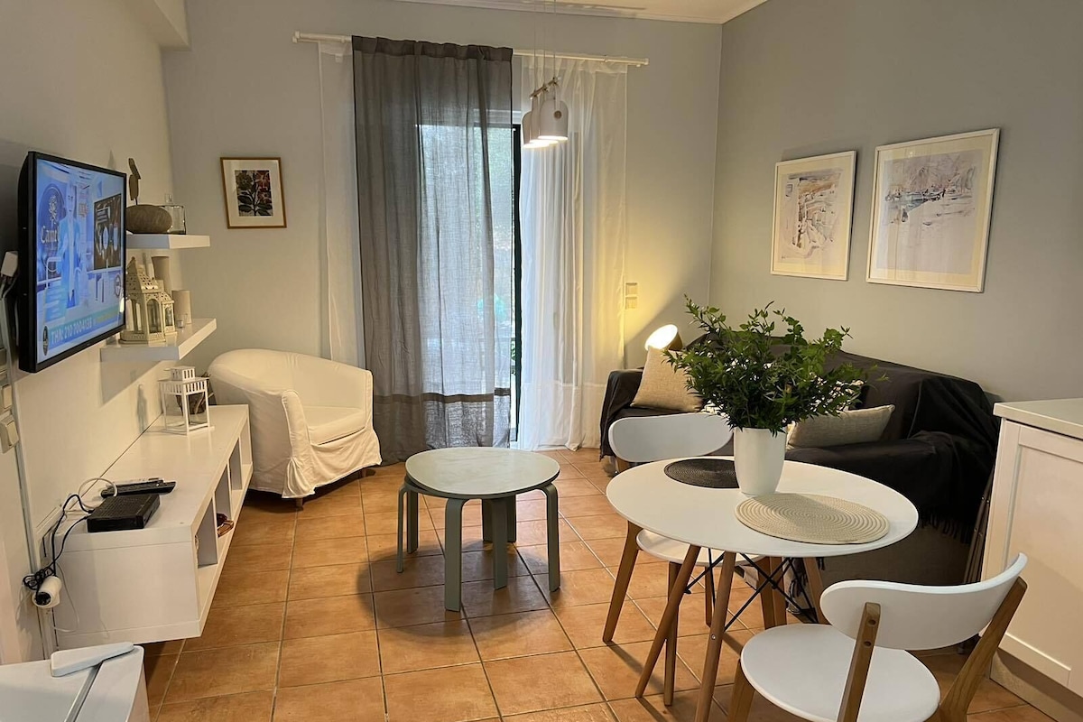 Un salon moderne avec un canapé, une table à manger et des chaises, un téléviseur fixé au mur et une plante en pot.
