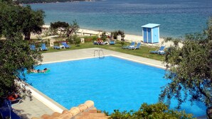 Ein Pool mit Blick auf das Meer und die Berge, umgeben von Liegestühlen und einem kleinen Gebäude.