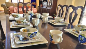 Une table à manger dressée avec des tasses et des soucoupes ornées de motifs floraux, des chaises en bois et un canapé en arrière-plan.