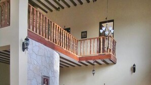 Un salon spacieux avec un haut plafond, un balcon en bois, une cheminée et un piano.