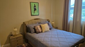 Een slaapkamer met een bed, nachtkastjes, een lamp en een schilderij aan de muur.