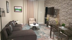 A living room with a sofa, a coffee table, a chair, and a dining area with a table and chairs.