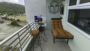 A balcony with a cushioned chair, a table with chairs, and a wall-mounted lamp.