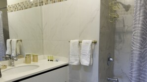 A modern bathroom with a white sink, mirror, and bathtub. There are towels on the wall and a shower curtain.