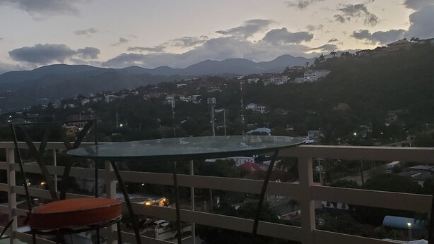 A balcony with two chairs and a table, overlooking a town with mountains in the distance.