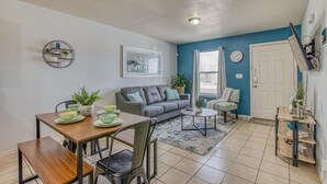 A living room with a dining table, sofa, and coffee table. There is a door, a clock, and a window with curtains. - ✨ BY FORT BLISS: 2 KING BEDS, FAST WIFI, FULL BATH, LAUNDRY (El Paso)