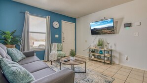 A living room with a sofa, coffee table, TV, and a plant shelf. - ✨ BY FORT BLISS: 2 KING BEDS, FAST WIFI, FULL BATH, LAUNDRY (El Paso)