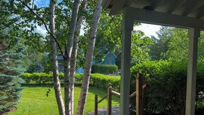 A wooden deck with a pergola, surrounded by lush greenery and a well-maintained lawn.