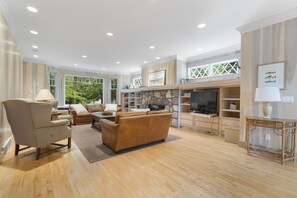 A spacious living room with a stone fireplace, a large flat-screen TV, and a comfortable seating area with a sofa and armchairs.
