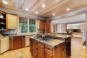 A spacious kitchen with wooden cabinets, granite countertops, and a central island with a stove.