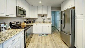 A kitchen with white cabinets, a stainless steel refrigerator, a microwave, and a stove. - Jewels Peace of Paradise (Rockport)