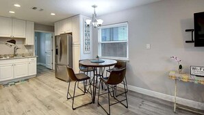 A modern kitchen with white cabinets, a stainless steel refrigerator, a dining table with four chairs, and a chandelier. - Jewels Peace of Paradise (Rockport)