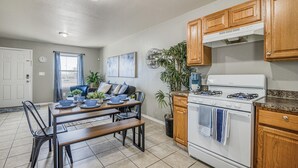 A kitchen with wooden cabinets, a white stove, and a dining area with a table and chairs. - ☕ BY FORT BLISS: LAUNDRY, SECURITY SYSTEM, REFRIGERATION, KING BEDS (El Paso)