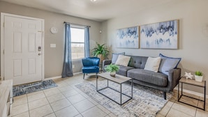 A living room with a grey sofa, a blue armchair, a coffee table, and two wall-mounted paintings. - ☕ BY FORT BLISS: LAUNDRY, SECURITY SYSTEM, REFRIGERATION, KING BEDS (El Paso)