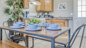 A dining area with a wooden table set for four, surrounded by chairs. A kitchen with wooden cabinets and a microwave is visible in the background. - ☕ BY FORT BLISS: LAUNDRY, SECURITY SYSTEM, REFRIGERATION, KING BEDS (El Paso)