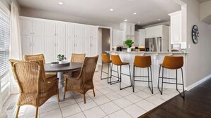 A modern kitchen with white cabinetry, a central island with bar stools, and a dining area with wicker chairs.
