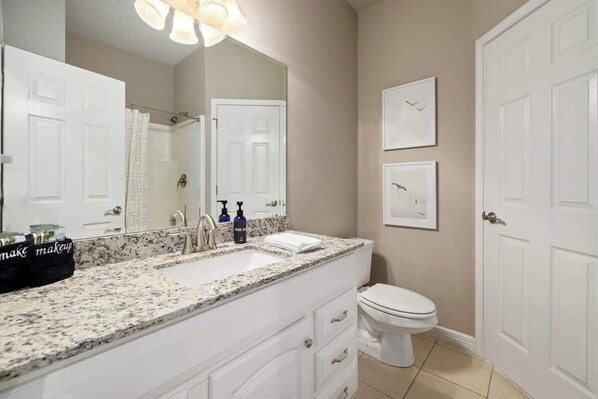 Un baño con lavamanos, encimera y tocador blancos, un inodoro y dos cuadros en la pared.