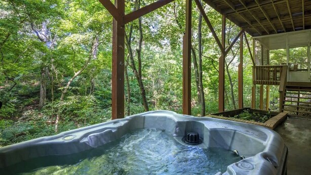 A hot tub surrounded by a wooden deck with a forest view.