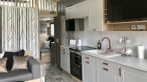 A compact kitchen with white cabinets, a built-in oven, and a large black TV mounted above the counter. - 2 Bed Lodge - Sleeps 4 - Parking - Wifi (Inverness)