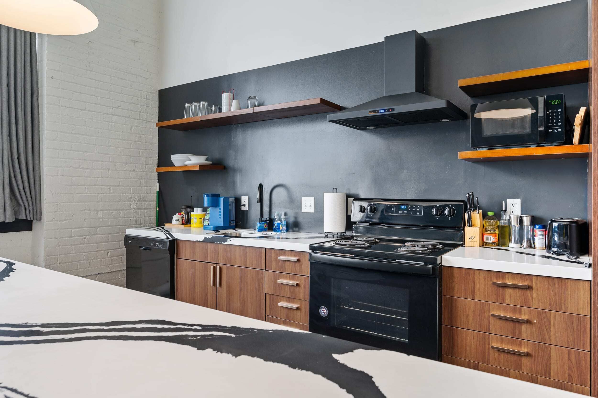 A modern kitchen with wooden cabinets, a black stove, a microwave, and a coffee maker.