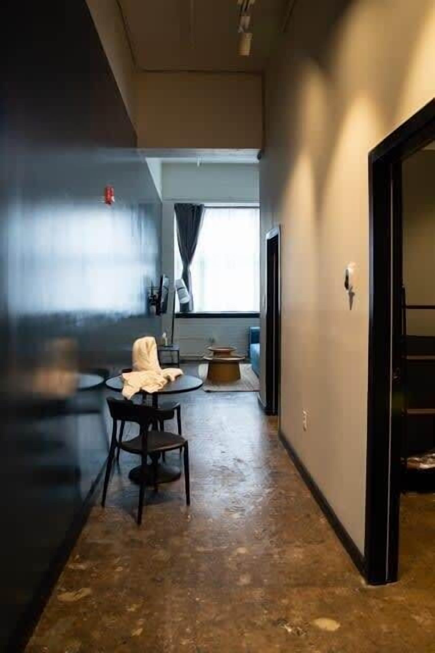 A narrow hallway with a round table and a chair, a small round table with a chair, and a door on the right.