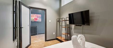 Habitación de hotel con cama, televisor montado en la pared, radiador y puerta que da a un pasillo.