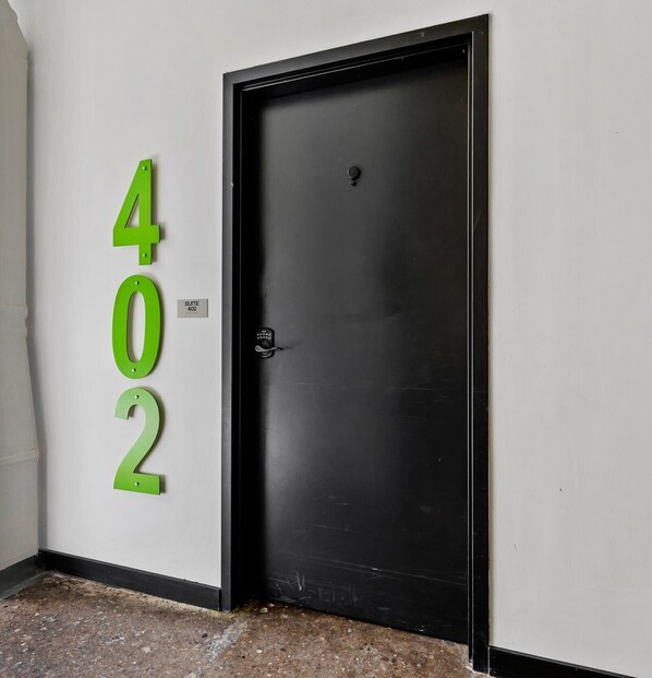 A black door with a keypad lock, adjacent to a wall with green numbers '402' and a sign indicating 'SUITE 402'.