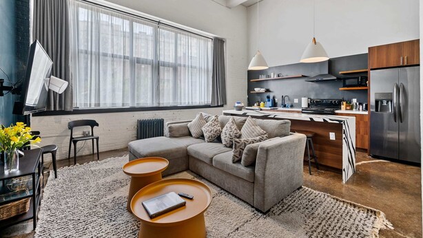 Una cocina moderna con un ventanal grande, un sofá gris y un comedor con una mesa pequeña y sillas.