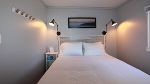 A bedroom with a bed, two bedside lamps, a nightstand, a framed picture on the wall, and a window.