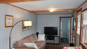 A living room with a sofa, a television, a lamp, and a wooden ceiling.