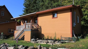 A wooden cabin with a balcony, a staircase, and a stone foundation.