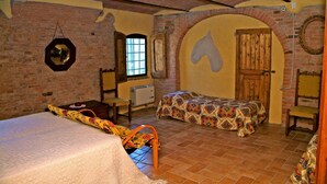 Una stanza con un letto, una sedia, un tavolino, una finestra e una porta decorata con un affresco a tema equestre.