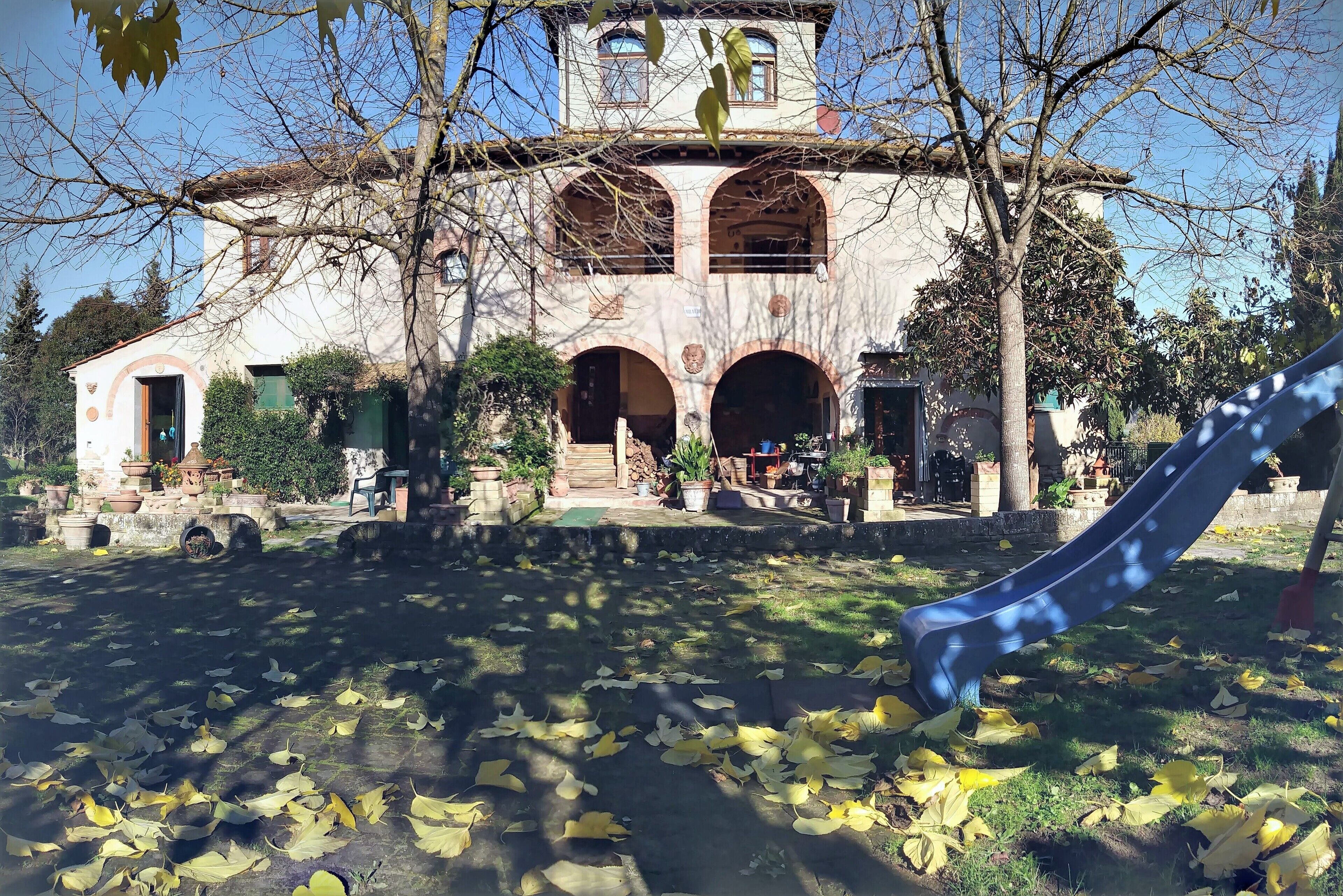Un bâtiment doté de fenêtres en arc de cercle et d’une tour, entouré d’arbres et d’une aire de jeux.