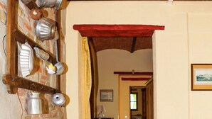 Un corridoio con una parete in mattoni, pentole di metallo su uno scaffale, una porta in legno e un quadro appeso al muro.