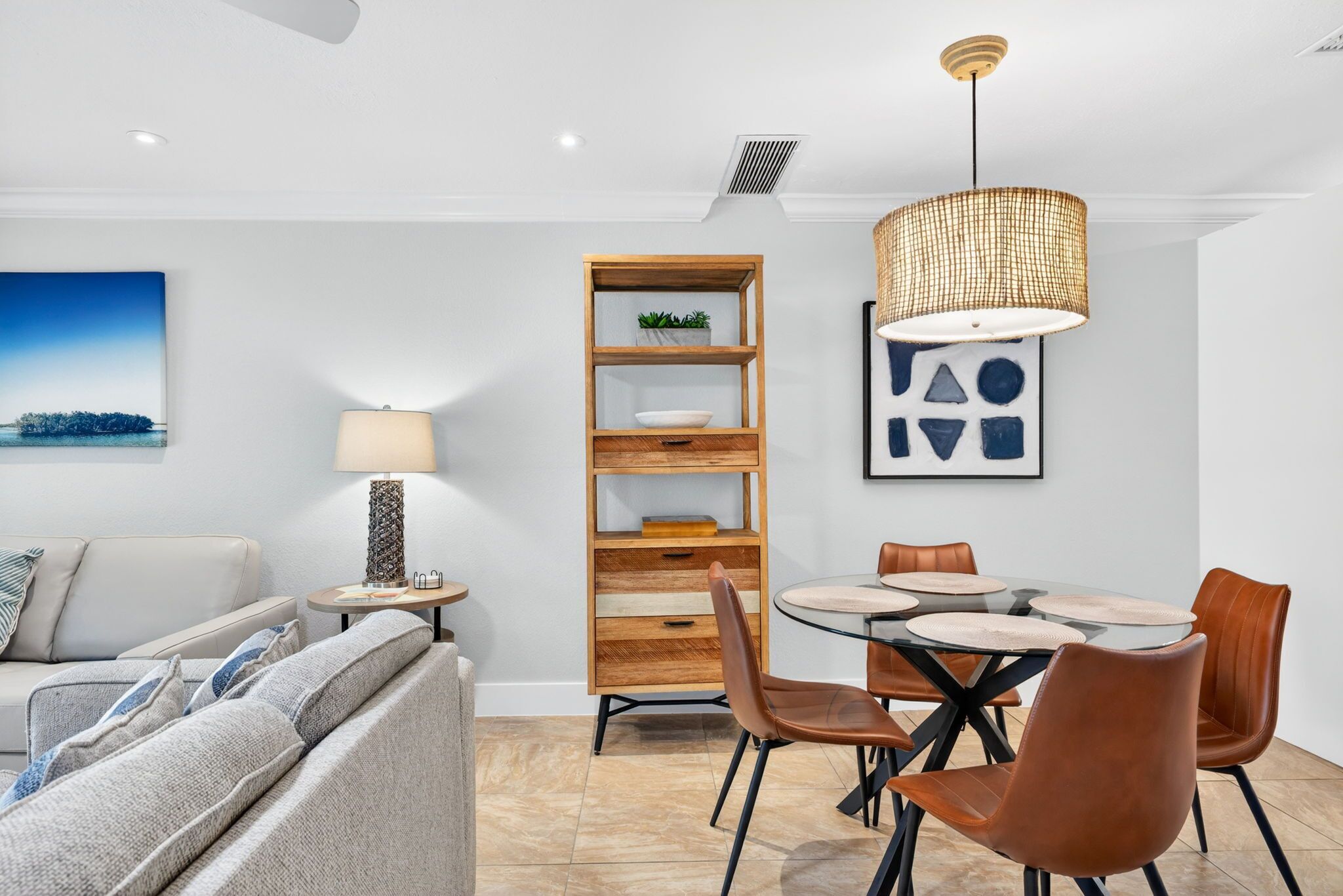 A modern living room with a sofa, a coffee table, a dining table with chairs, a lamp, a bookshelf, and a pendant light.