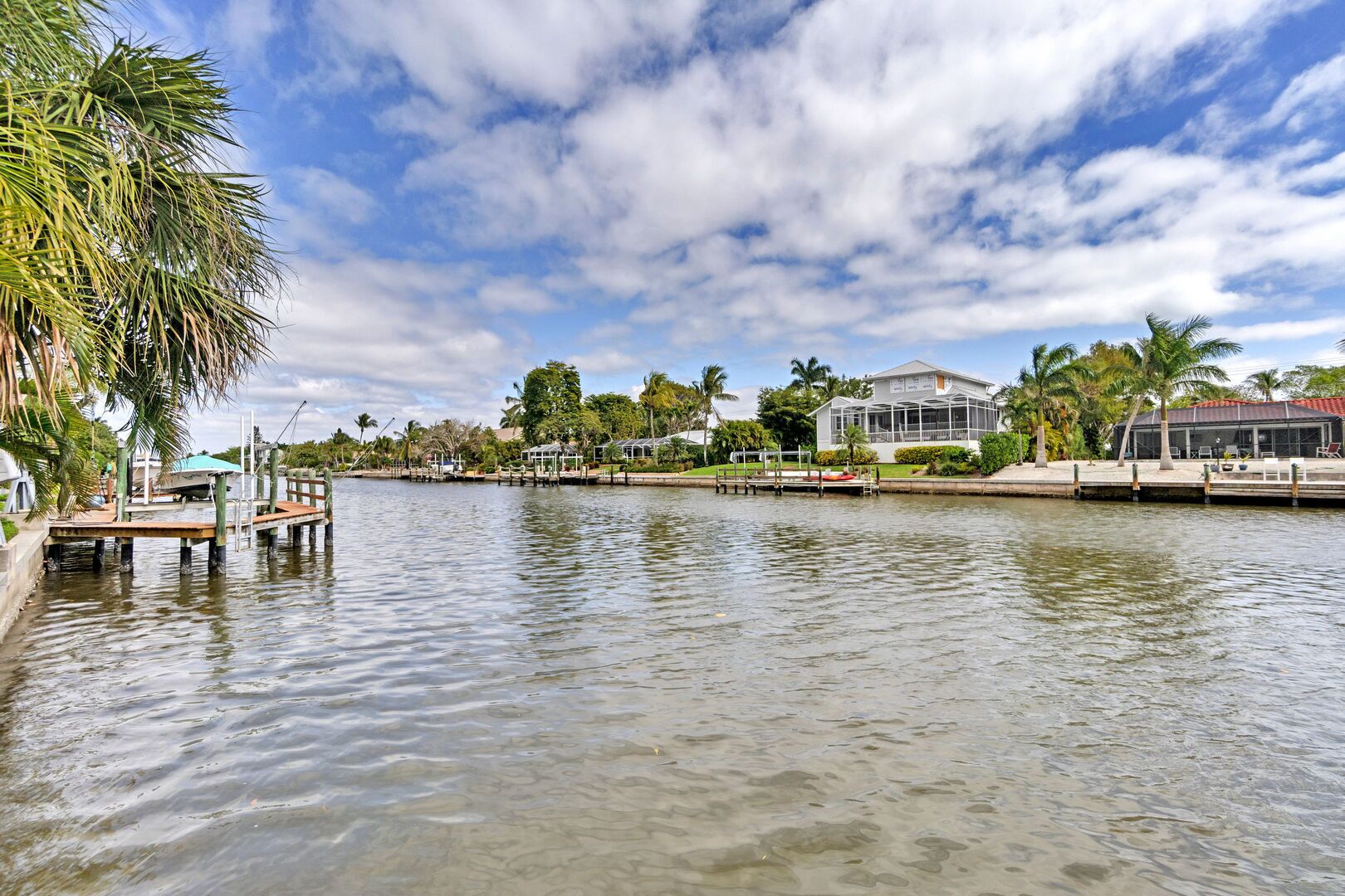 A waterfront property with a dock, a house with a screened porch, and palm trees.