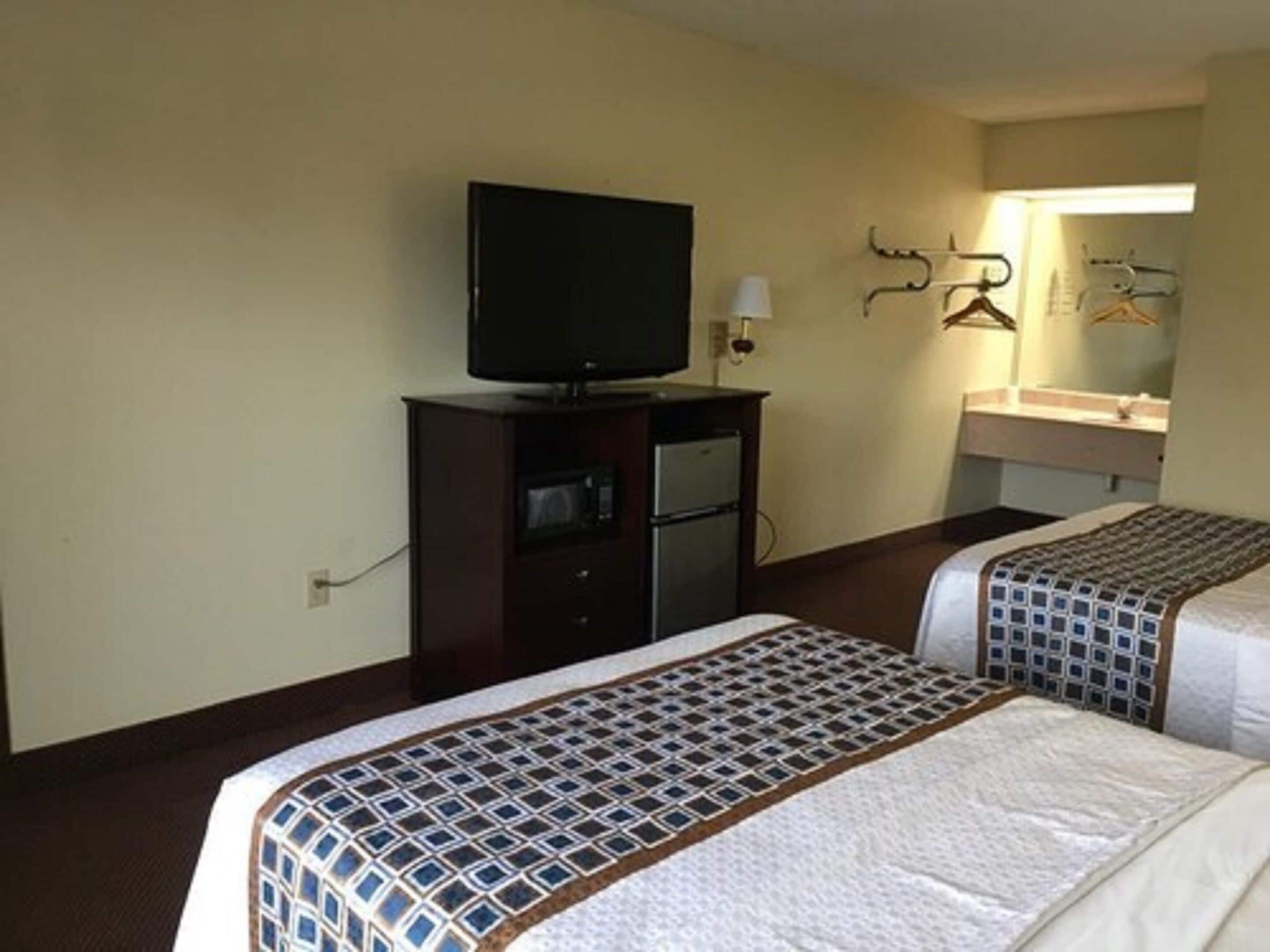 A hotel room with two beds, a television on a cabinet, a microwave, and a bathroom with a mirror and towel rack.