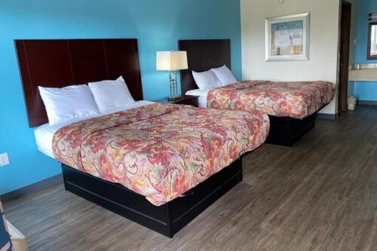 A hotel room with two beds, a nightstand, a lamp, and a framed picture on the wall.