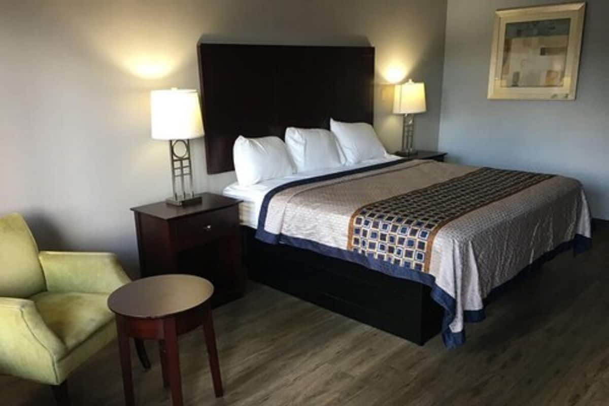 A hotel room with a bed, two bedside lamps, a small round table, a chair, and a framed picture on the wall.