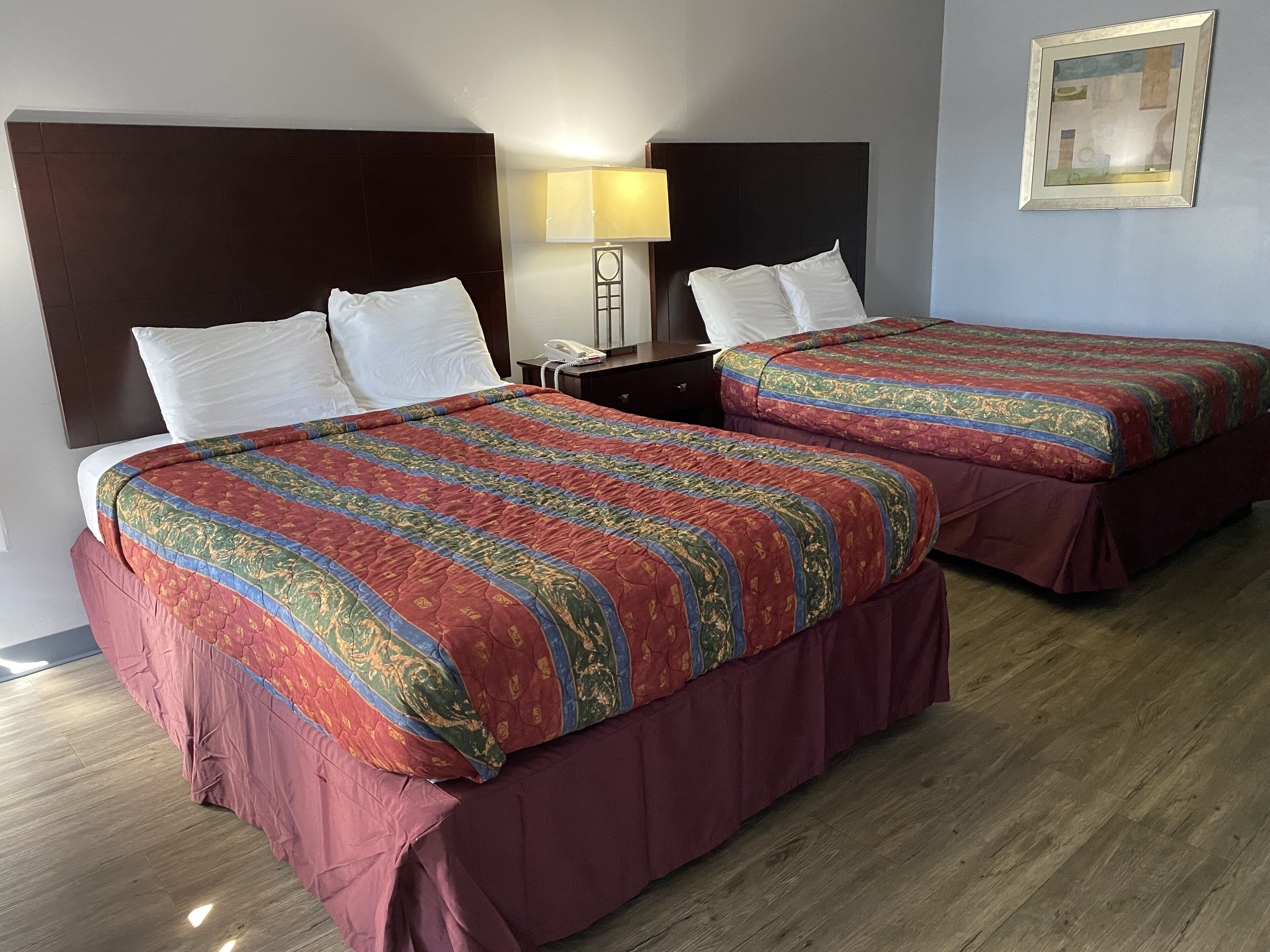 Two double beds with matching headboards and footboards, a bedside table with a lamp, and a framed picture on the wall.