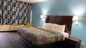 A hotel room with a large bed, two bedside lamps, a wooden nightstand, and a floral curtain. - Havelock Inn & Suites (Havelock)