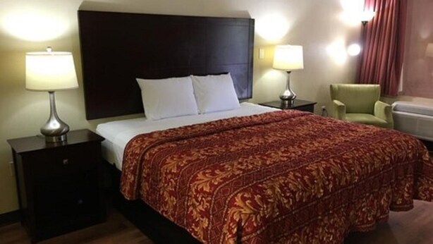 A hotel room with a large bed, two bedside tables with lamps, a green armchair, and a dark headboard. - Havelock Inn & Suites (Havelock)