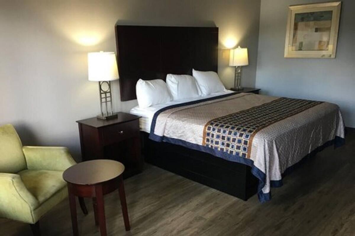 A hotel room with a bed, two bedside lamps, a chair, and a small table.
